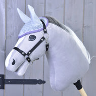 A light gray hobby horse with a white mane, wearing a black bridle and the Hobby Horse LarDen Ear bonnet crocheted Candy for insect protection, is positioned against a wooden panel background.
