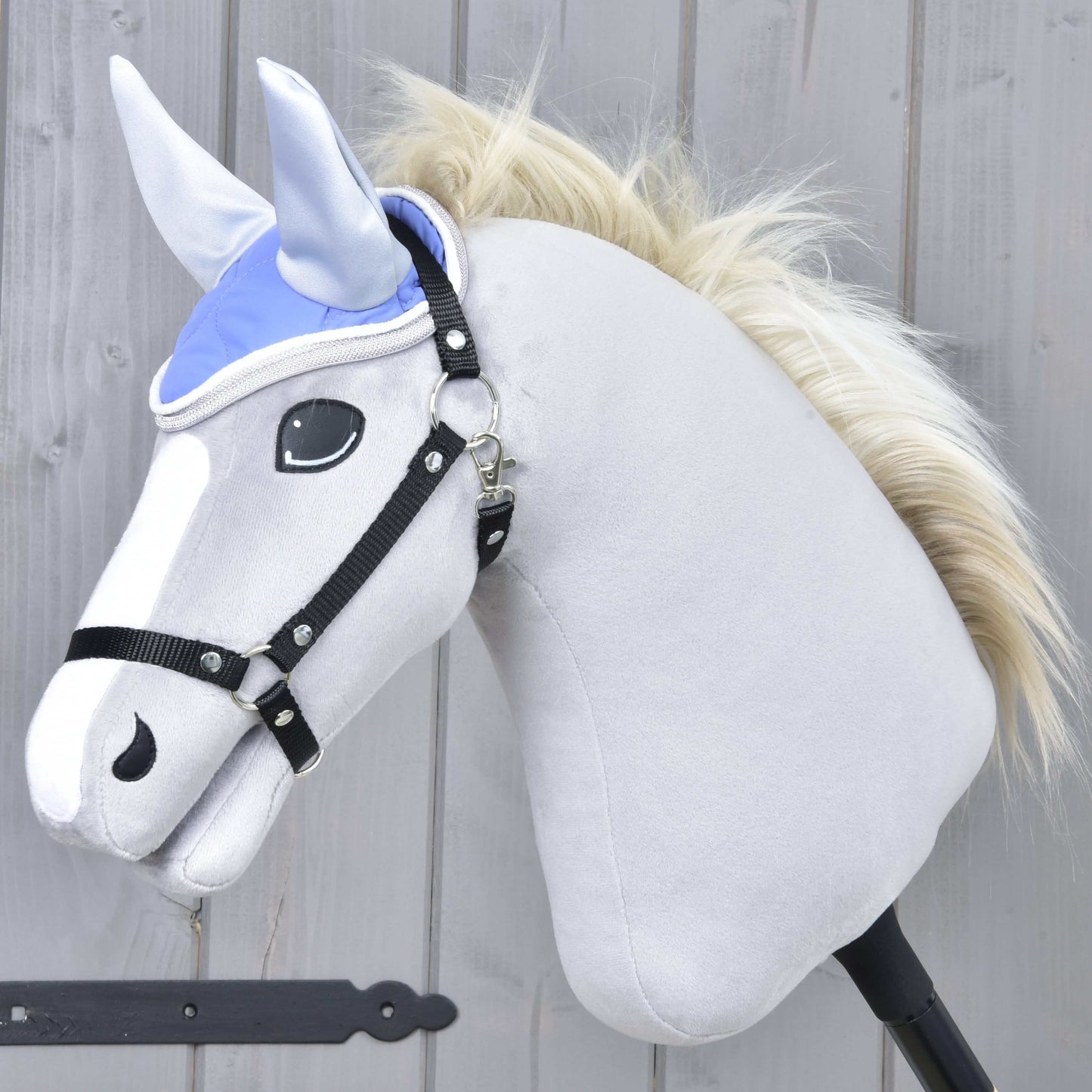 Bonnet d'oreilles violet clair de Hobby Horse LarDen sur un Hobby Horse en peluche gris clair avec crinière blanche et bride noire, sur fond en bois.