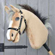 Hobby Horse Caramel mit Schwarzem Halfter von Hobby Horse LarDen mit beigefarbenem Gesicht, schwarzer Mähne und weißen Details, auf einem Holzstock vor einer grauen Holzwand.