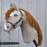 Hobby Horse Chanell mit Schwarzem Halfter von Hobby Horse LarDen mit weichem Plüschkörper, schwarzem Halfter, weißen Gesichtsabzeichen, brauner Garnmähne und Comic-Augen, gezeigt vor einer hellgrauen Holzwand.