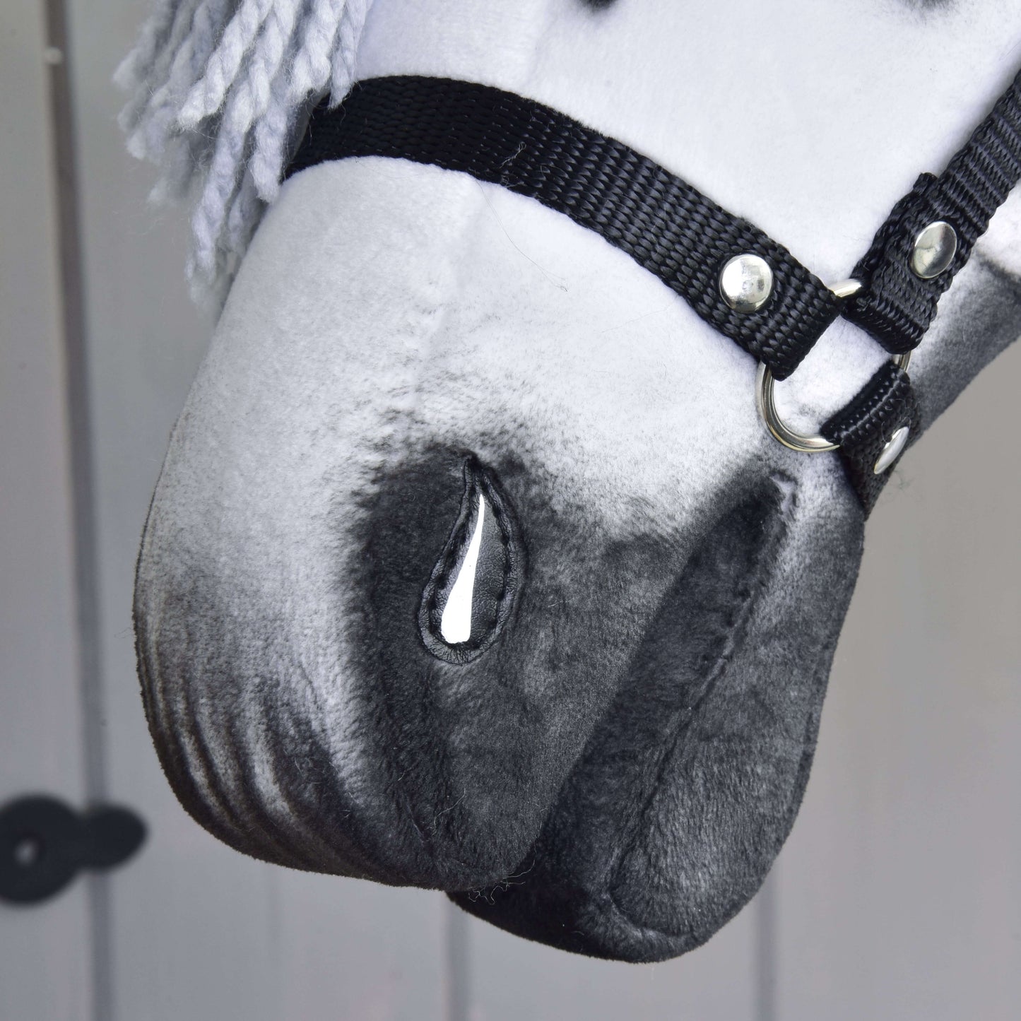 Gros plan sur Hobby Horse Chantal avec licol noir de Hobby Horse LarDen, fabriqué à la main, avec coloris blanc et gris, détail peint en forme de larme, crinière en fil et fond neutre.
