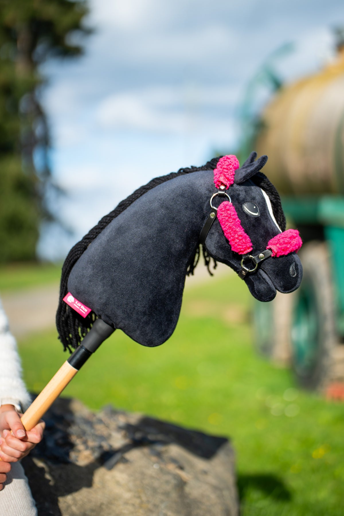 Kopf und Hals des Hobby Horse Cloony mit schwarzem Halfter von Hobby Horse LarDen werden vor bewölktem Himmel hochgehalten – schwarzer Plüsch, weißer Stern, schwarze Garnmähne – hier mit dem schwarzen Kunstlederhalfter mit vollständigem rosa Fell