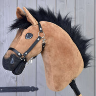 Nahaufnahme von Hobby Horse Cookie mit Schwarzem Halfter von Hobby Horse LarDen mit einem braunen Plüschpferd mit schwarzer Mähne und Halfter, glänzenden Augen und grauem Holz Hintergrund.