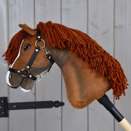 Hobby Horse Cooper mit schwarzem Halfter von Hobby Horse LarDen mit braunem Stoffkopf, Garnmähne und weißer Blesse auf der Nase, montiert auf einem Holzstab. Im Stil eines eleganten Sportpferdes gestaltet, ist es ideal als fantasievolle Dressurabenteuer und hier vor einem grauen Holzhintergrund fotografiert.