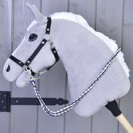 Rênes Cremo/Bleu de Hobby Horse LarDen, Hobby Horse en peluche grise avec crinière blanche, bride noire, rênes faites main, éléments métalliques argentés et corde tressée bleue et blanche sur un bâton en bois, présenté devant un mur en bois gris.