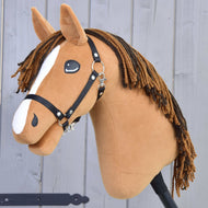 Hobby Horse Edward-LD mit Schwarzem Halfter von Hobby Horse LarDen, ein fuchsfarbener Hengst mit weißer Blesse und brauner Garnmähne, auf einem Stock vor einer grauen Holzwand.