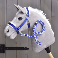 The Hobby Horse LarDen Set Essential Blue features a gray plush hobby horse with a white mane, blue fur-trimmed halter, and blue-and-white rope rein on a wooden stick, shown in front of a gray wooden fence.