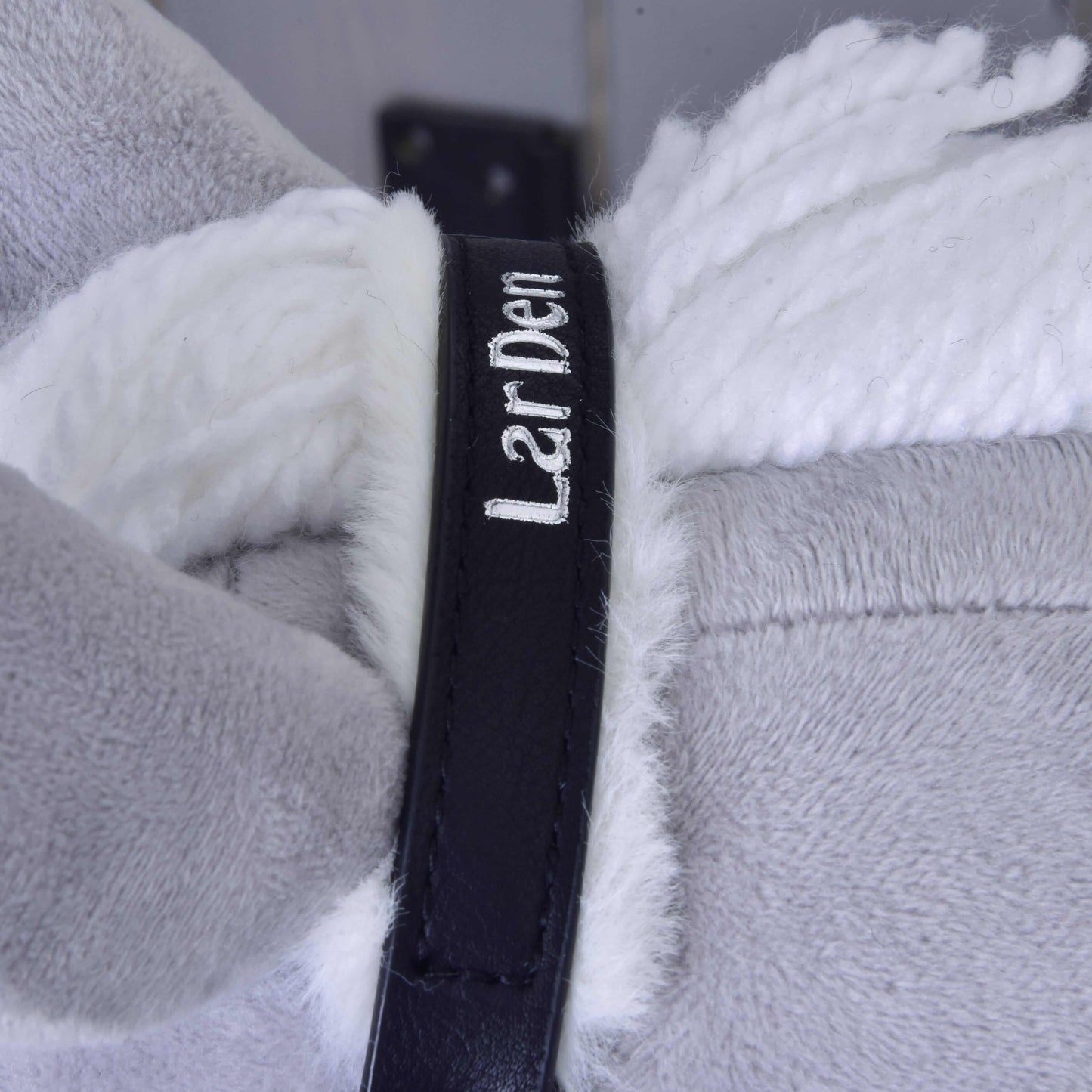 Close-up of a black strap with white LarDen text, wrapped around plush light grey and white fur—perfect as a Hobby Horse LarDen Halter with Fur in leatherette Espresso.