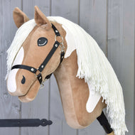 Hobby Horse Fury mit Schwarzem Halfter von Hobby Horse LarDen mit plüschigem hellbraun-weißem Gesicht, langer weißer Mähne, schwarzem Halfter und auf einem Stab, bereit für Ausritte vor grauem Holz-Hintergrund.