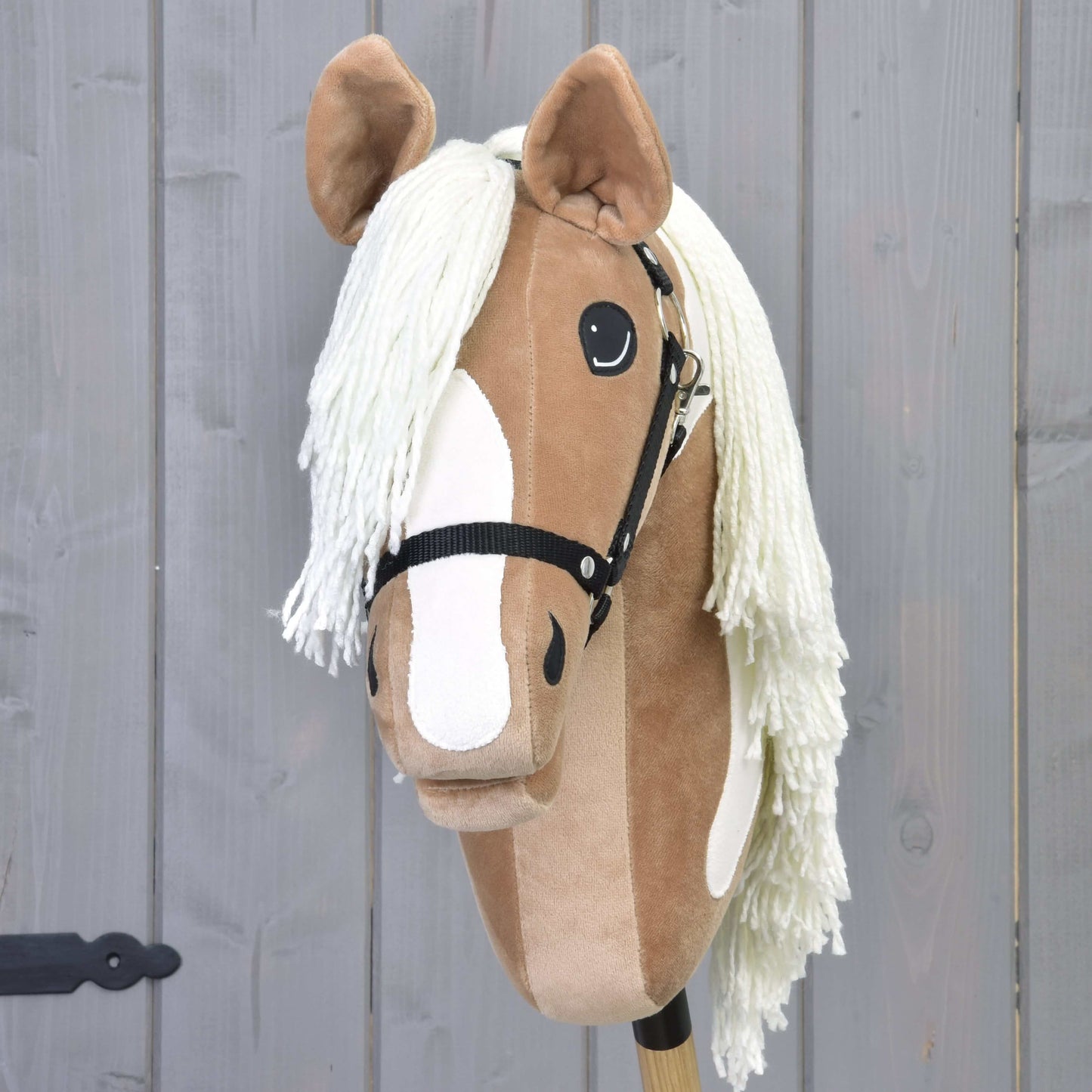 Hobby Horse Fury avec licol noir de Hobby Horse LarDen, avec visage beige et blanc, licol noir et longue crinière blanche, ressemblant à un American Paint Horse, sur fond en bois gris. Idéal pour des aventures imaginatives.