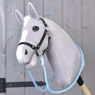 Zügel Heaven von Hobby Horse LarDen ist ein graues Plüsch-Hobby Horse mit weißer Schnauze, schwarzem Zaumzeug und blauen Zügeln aus Polypropylenseil, auf einem Holzstab montiert und vor Holzvertäfelung gezeigt.