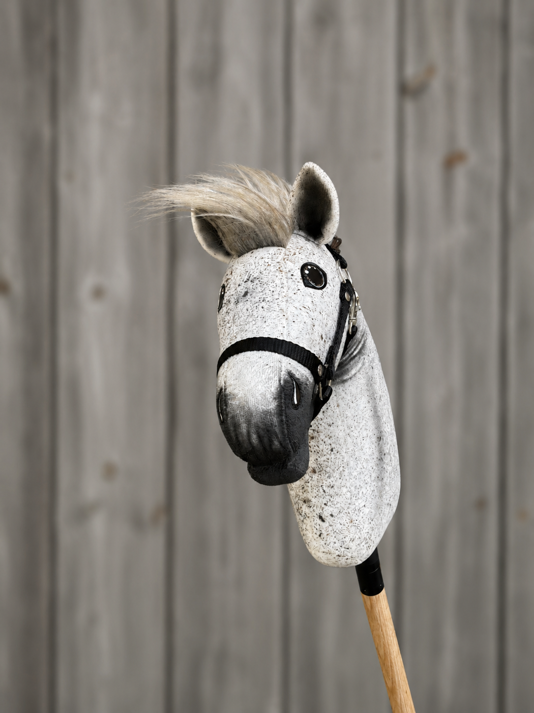 The Hobby Horse LarDen "Hobby Horse Luna with Black Halter" (size S) features a gray plush Appaloosa head, black halter, and wooden stick handle, displayed against a gray wooden plank background.