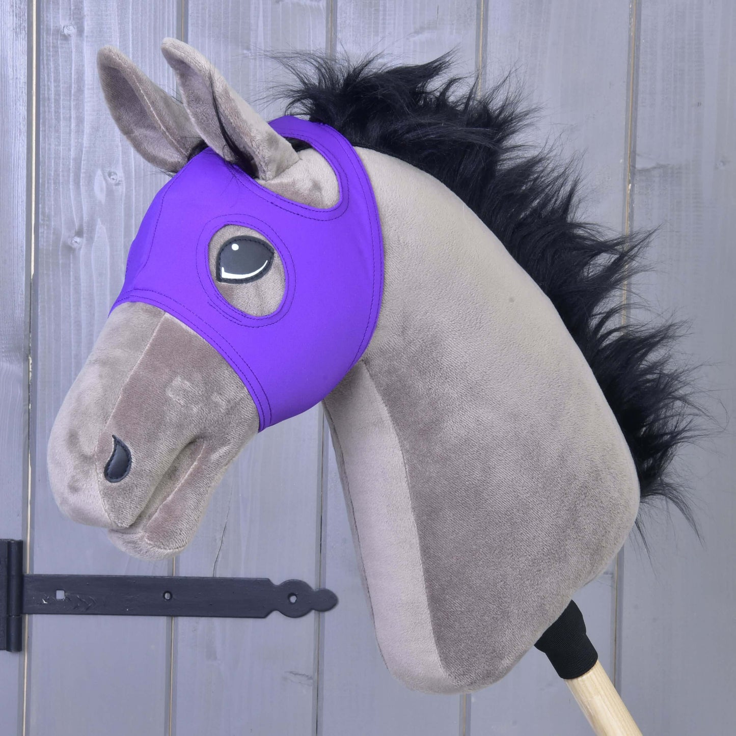 Maske ohne Ohren Indigo von Hobby Horse LarDen an einem Plüsch-Hobby Horse mit schwarzer Mähne und grauem Gesicht, aus waschbarem PES-Material, auf einem Holzstab vor einer grauen Holzwand.