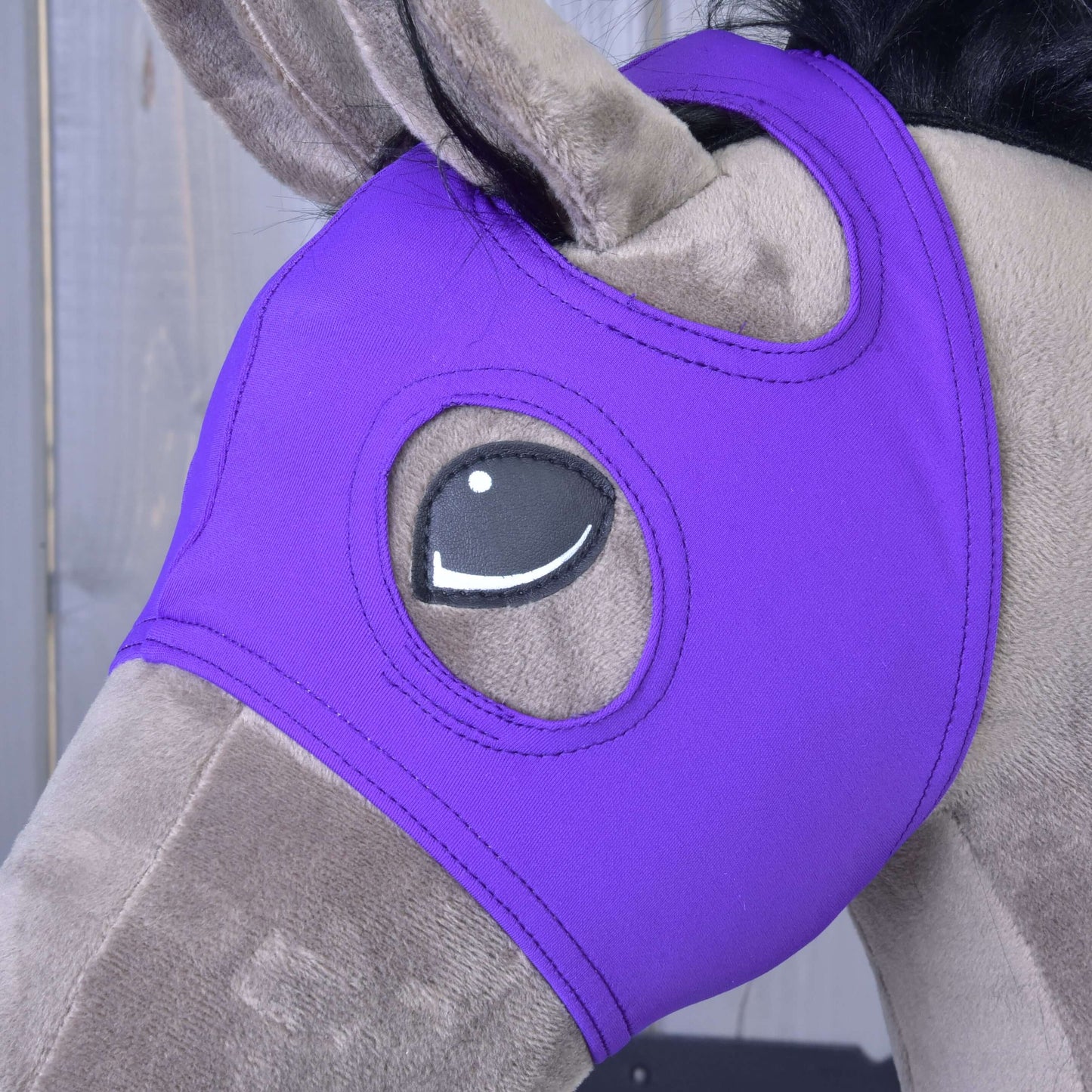 Maske ohne Ohren Indigo von Hobby Horse LarDen aus waschbarem PES an einem Plüschpferd, bedeckt den Kopf mit Augenöffnungen, vor einem Holzhintergrund.