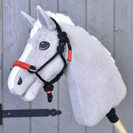 Hobby Horse LarDen Seilhalfter Funke auf einem grauen Hobby Horse mit weißer Mähne und schwarz-rotem Seilhalfter, auf einem Holzstab vor einer grauen Holzwand.