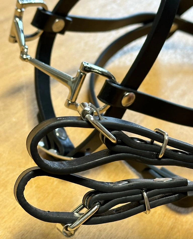 Close-up of black leather horse bridle and reins with shiny silver metal buckles and rings, perfect for a Hobby Horsing setup, resting on a light brown surface.