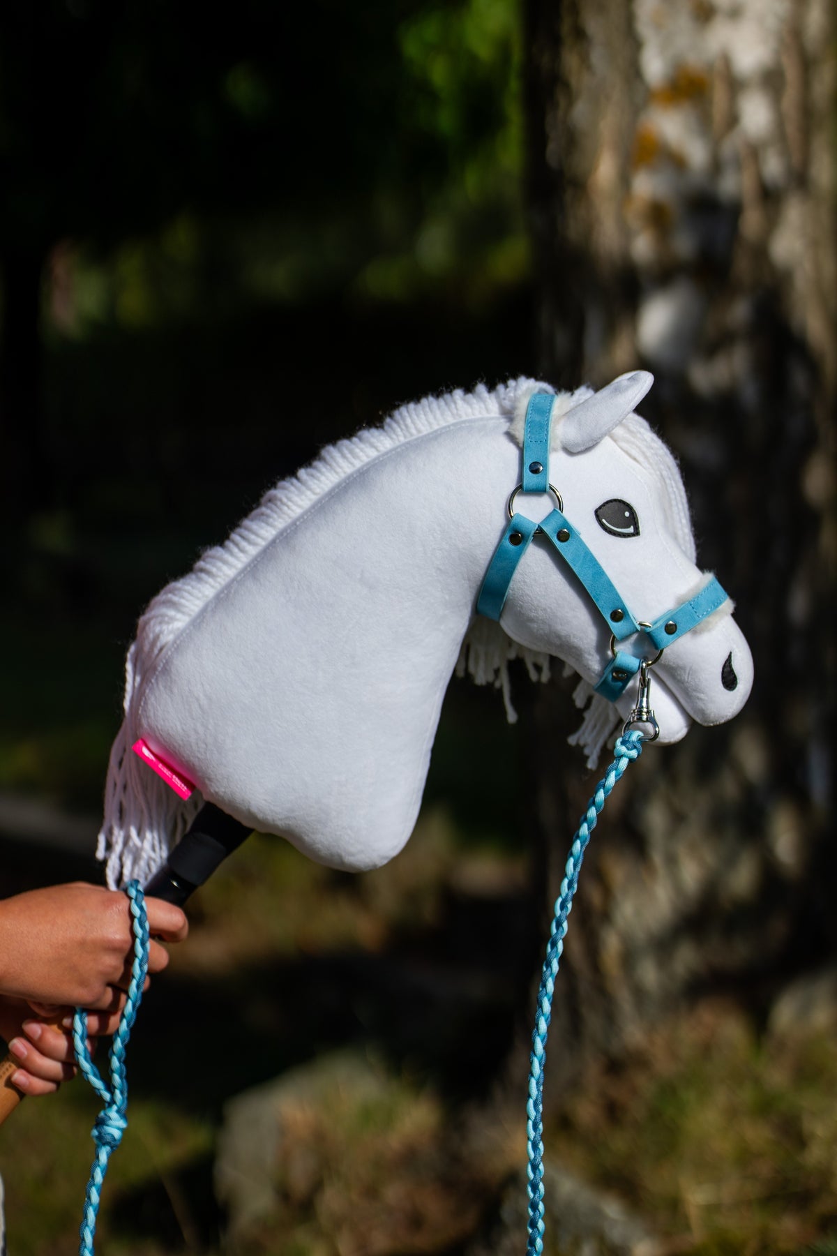 Weißes Hobby Horse mit pastellblauem Fellhalfter und geflochtenem blauem Führstrick im Freien