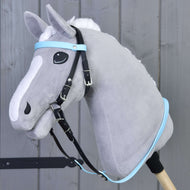 A gray plush hobby horse with a white mane, fitted with the Hobby Horse LarDen Complete bridle without noseband in Light Blue, mounted on a wooden stick and pictured before a gray wooden wall.