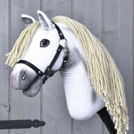 Hobby Horse Little Lady mit Schwarzem Halfter von Hobby Horse LarDen mit weißem Körper und langer cremefarbener Garnmähne, vor Holzpanelen, inspiriert von der Eleganz der Dressur des Pura Raza Española.