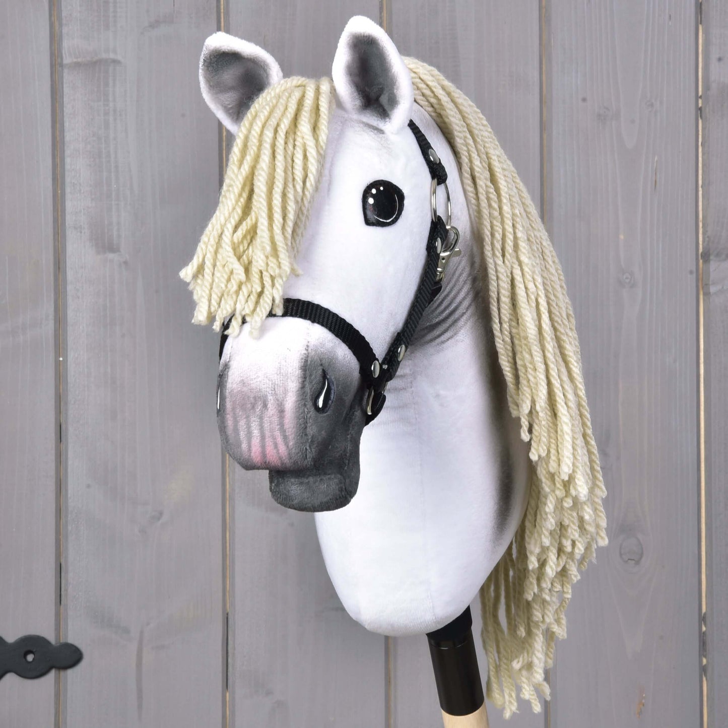 Hobby Horse Little Lady mit Schwarzem Halfter von Hobby Horse LarDen mit schwarzem Halfter, großen schwarzen Augen und langer hellblonder Garnmähne auf einem Stock – perfekt für fantasievolles Dressurspiel vor hellem Holzhintergrund.