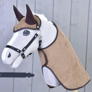 Das Set Manchester Le Chocolate von Hobby Horse LarDen zeigt ein Plüsch-Hobby Horse mit weißem Gesicht, schwarzem Zaumzeug, braunen Ohren und strukturiertem braunem Stoff an Kopf und Hals, mit einer Hobby Horse Decke auf einem Holzstab vor einer grauen Holzwand.