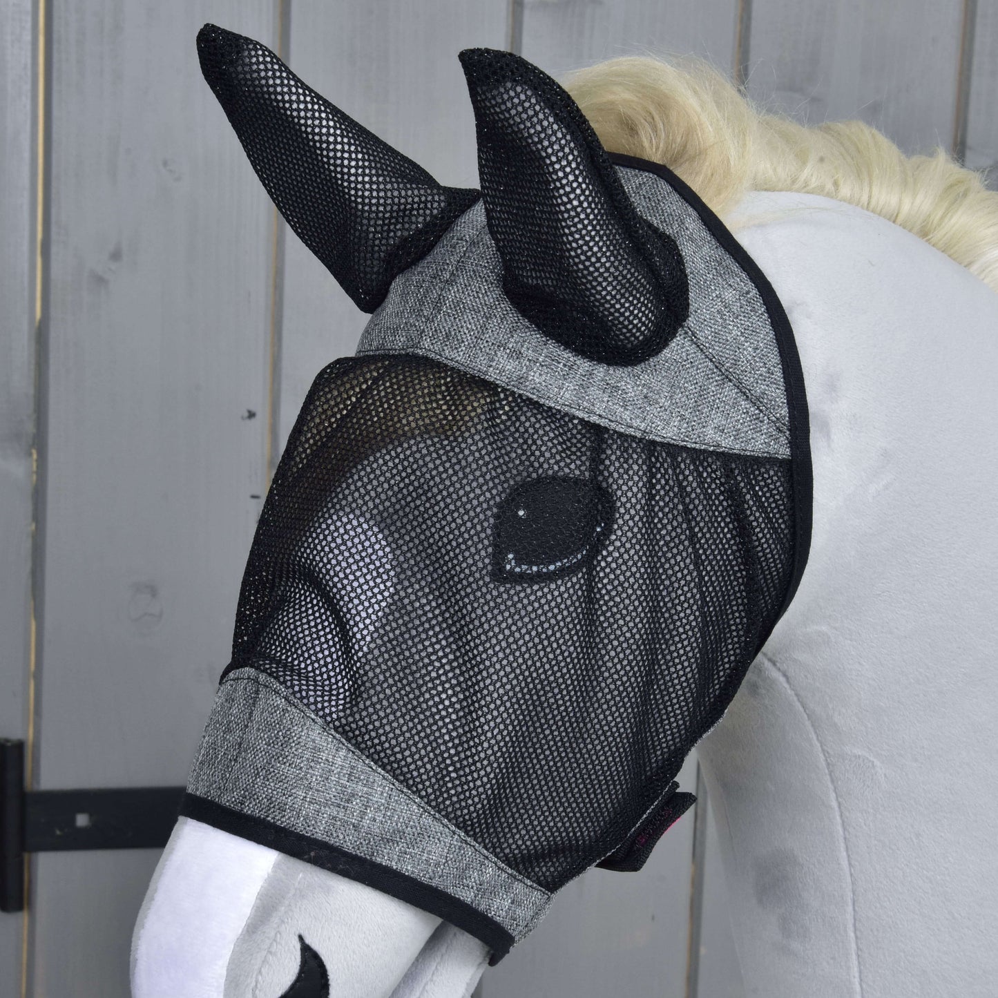 Mannequin de cheval blanc portant le Masque anti-mouches De Luxe Gris Clair de Hobby Horse LarDen, qui couvre les oreilles et les yeux, devant un fond en bois.