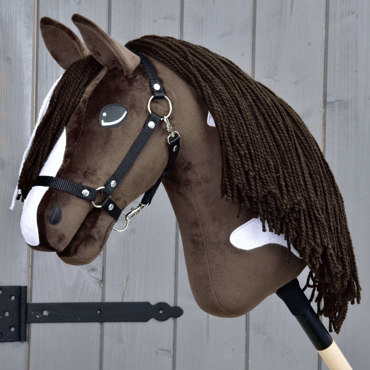 Hobby Horse Monte mit Schwarzem Halfter von Hobby Horse LarDen zeigt ein braun-weißes Design, inspiriert vom American Paint Horse, mit schwarzem Halfter für Hobby Horse, weißen Flecken, langer dunkler Garnmähne und auf einem Holzstab montiert.