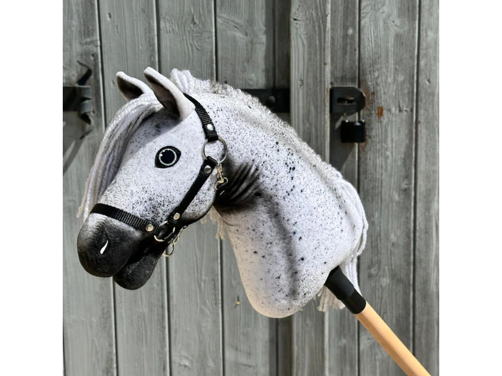 Hobby Horse Naivy mit schwarzem Halfter von Hobby Horse LarDen vor einer rustikalen Holztür, mit grau-weißem Appaloosa-Design und detaillierter Mähne.