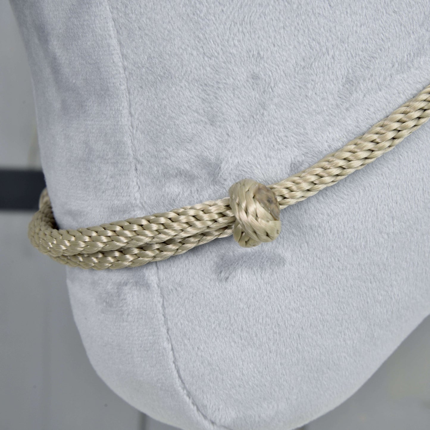 Nahaufnahme des Halsring Eleganza von Hobby Horse LarDen, ein dickes, hellbeiges geflochtenes Seil, das mit einem Knoten um ein weiches weißes Kissen gebunden ist, und den auffälligen Kontrast zwischen dem Halsring und dem samtigen Stoff hervorhebt.