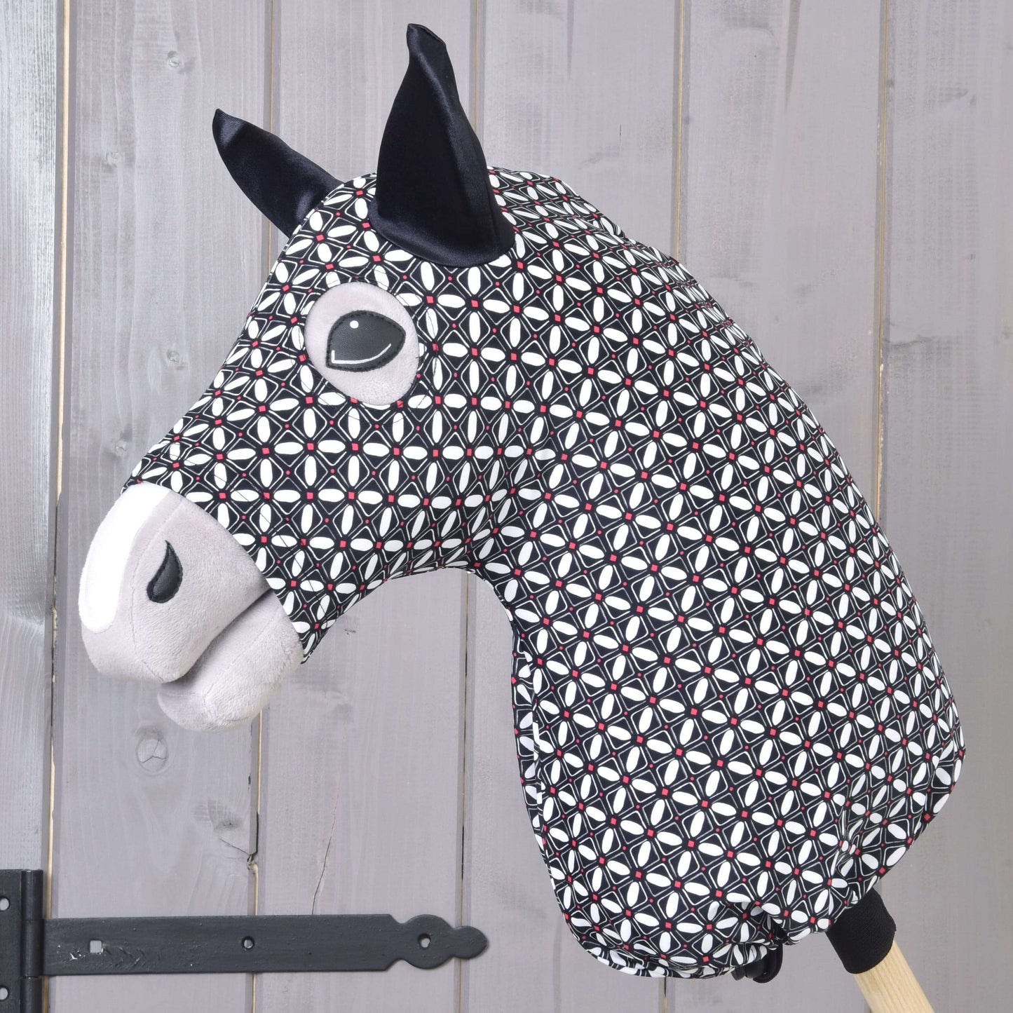 Hobby Horse Schutzanzug DeLuxe (Lycra) von Hobby Horse LarDen mit schwarzem, weißem und rotem geometrischem Stoff, schwarzen Ohren und gestickten Gesichtsdetails, vor einem Hintergrund aus hellen Holzpaneelen gezeigt.