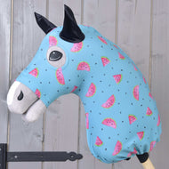 Hobby Horse Schutzanzug Melon (Lycra) von Hobby Horse LarDen mit waschbarem blauem Bezug mit pinken Wassermelonenscheiben und schwarzen Kernen, entworfen für Plüschköpfe von Hobby Horse. Ideal als Schutz, gezeigt auf einem Holzstab vor einer hellen holzvertäfelten Wand.