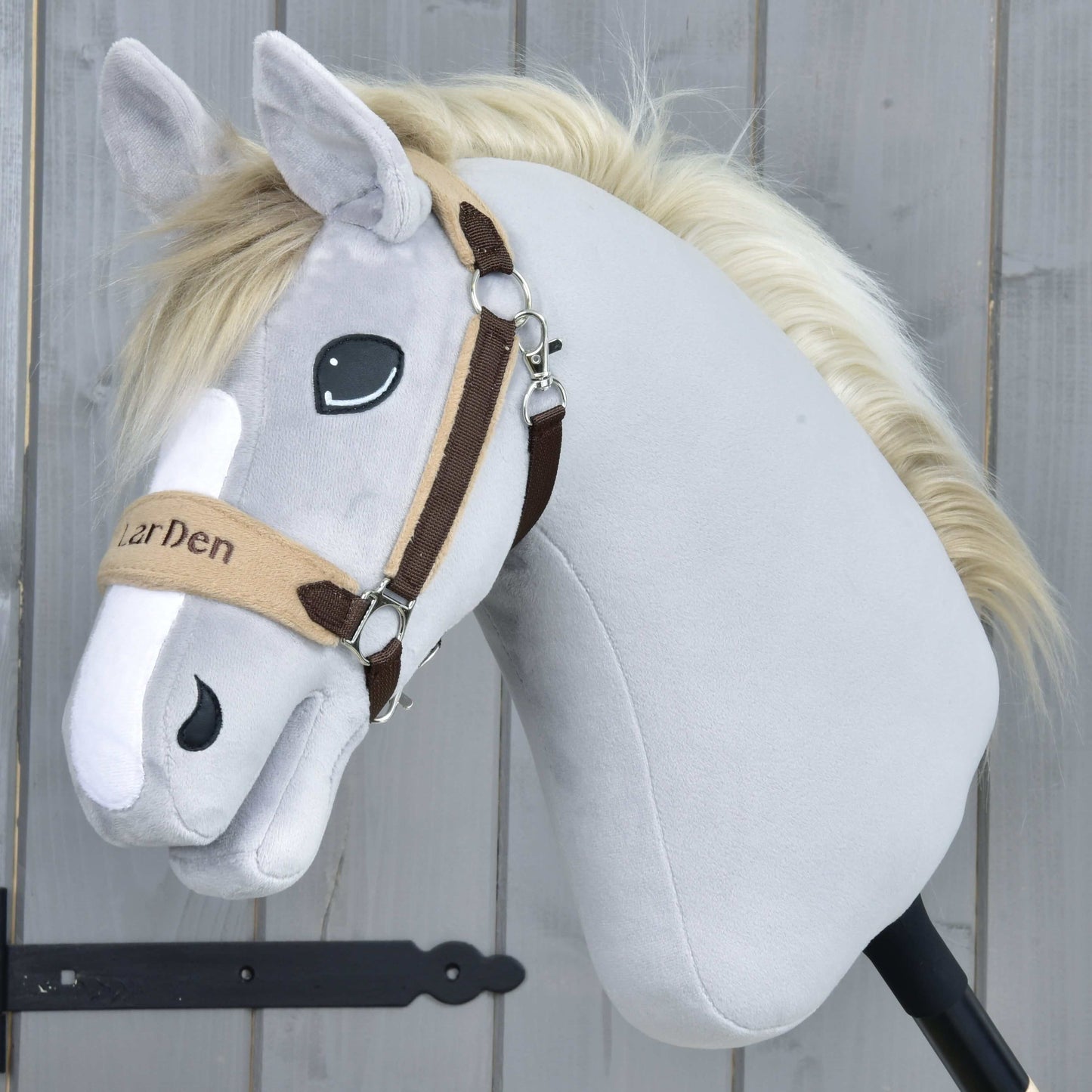 Hobby Horse LarDen « Licol en fourrure LarDen marron », avec fourrure en peluche gris clair, crinière crème, licol beige et marron avec muserolle douce en polaire, yeux brodés et expression amicale, sur fond en bois.