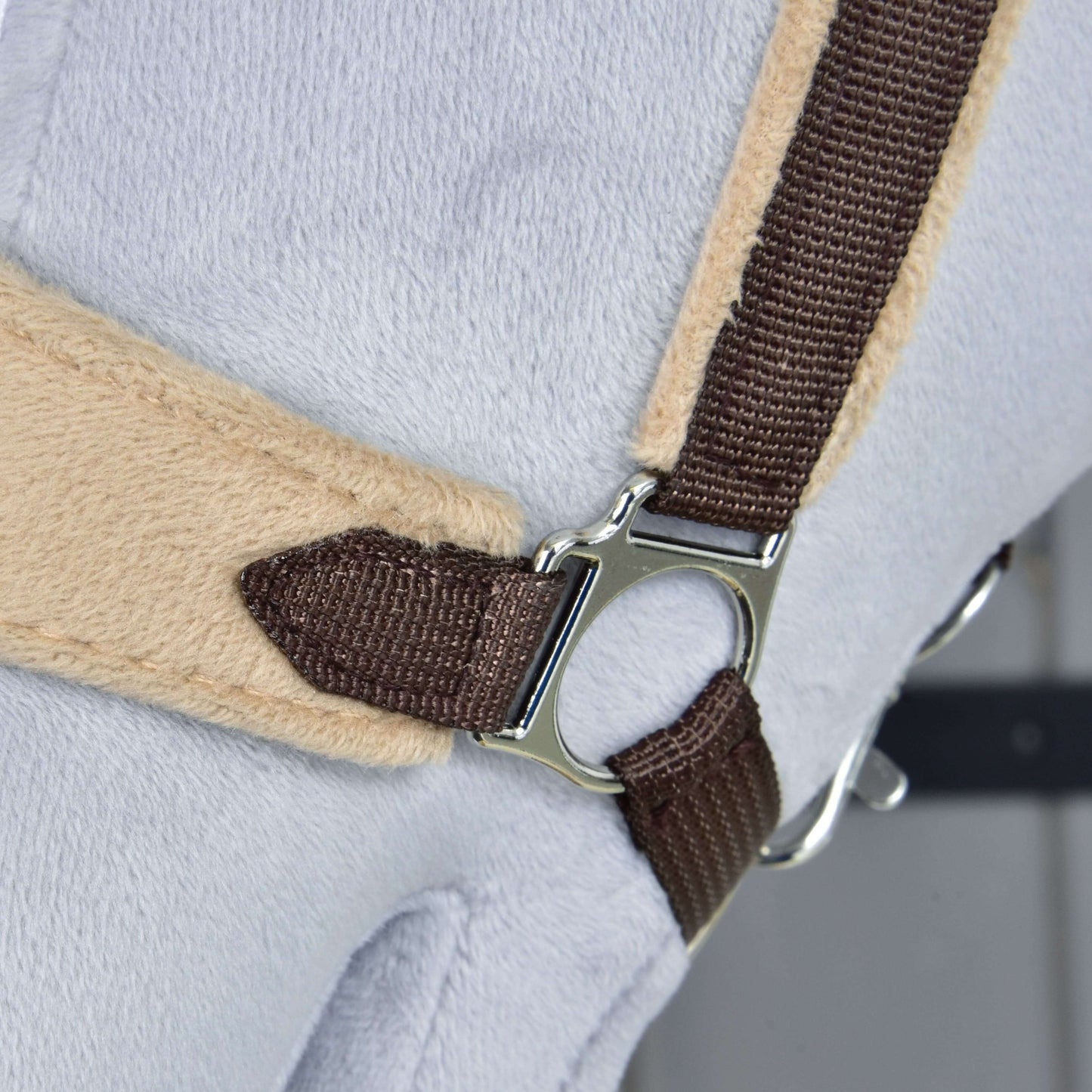 Gros plan sur le Licol en fourrure LarDen marron de Hobby Horse LarDen, avec sangle marron, anneau métallique et muserolle douce en polaire sur une surface gris clair et beige, ressemblant à une partie d’un accessoire en peluche pour Hobby Horse.