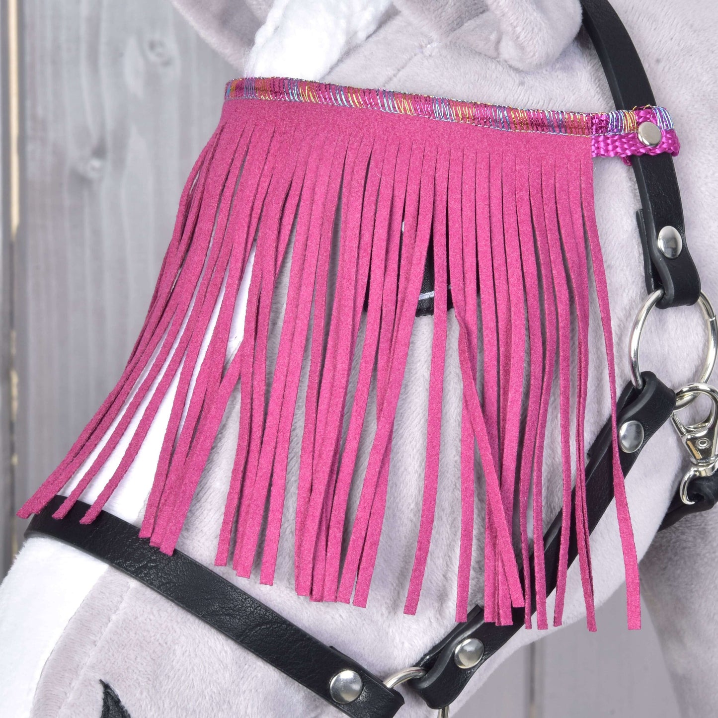 Gros plan d’un « Licol noir avec franges roses » de Hobby Horse LarDen sur une tête de Hobby Horse en peluche. Les franges rose vif décorent le visage, avec un fond en bois.