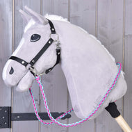 Das Hobby Horse LarDen „Zügel Pinkie Blue“ ist ein graues Plüsch-Hobby Horse mit schwarzem Zaumzeug und handgeflochtenen Zügeln in Pink, Blau und Weiß an einem Holzstab, gezeigt vor hellem Holz-Hintergrund.
