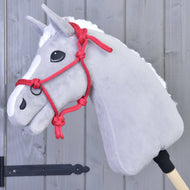Ein graues Hobby Horse LarDen mit weißer Mähne, schwarzen Augen und einem leuchtend roten Seilhalfter, Seilhalfter Rot, ist auf einem Holzstab montiert und vor einer grauen Holzwand positioniert.