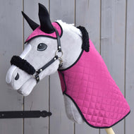 The Hobby Horse LarDen Set Pink Beauty features a plush toy hobby horse with a quilted pink blanket, matching ear bonnet, and a fur-trimmed halter—essential accessories—posing before wooden planks.