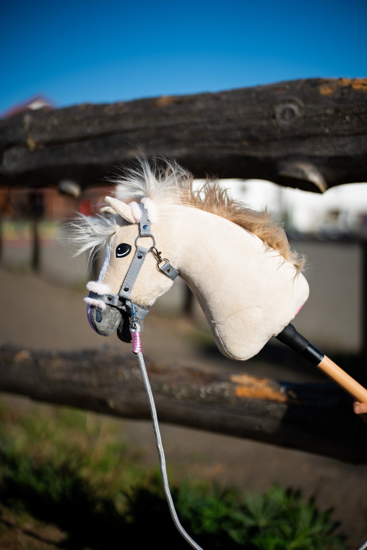 Detail photo: the head of the Hobby Horse Pixie with Black Halter by Hobby Horse LarDen in front of a wooden paddock fence - beige plush, white yarn mane - shown here with the Halter grey with pink fur and the grey and pink rope stripe Tizian lead.