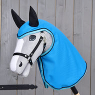 Hobby Horse LarDen Regendecke Sky Blue an einem grau-weißen Hobby Horse mit schwarzen Zügeln und Ohren, das eine glänzende himmelblaue Kapuze im Regendecken-Stil trägt, vor Holz-Hintergrund.