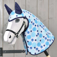 Hobby Horse LarDen Regendecke Bubbles mit weißem Gesicht, schwarzem Zaumzeug, blauen Ohren und hellblau gepunkteter Decke mit Allwetter-Accessoires auf einem Holzstock, vor einer Holzwand.