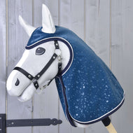 Die Hobby Horse LarDen "Regendecke Derby" ist ein weißes plüschiges Hobby Horse mit schwarzem Halfter für Hobby Horse und glänzendem blauem Regenmantel mit Wassertropfenmuster, präsentiert vor einem Hintergrund aus hellen Holzplanken.