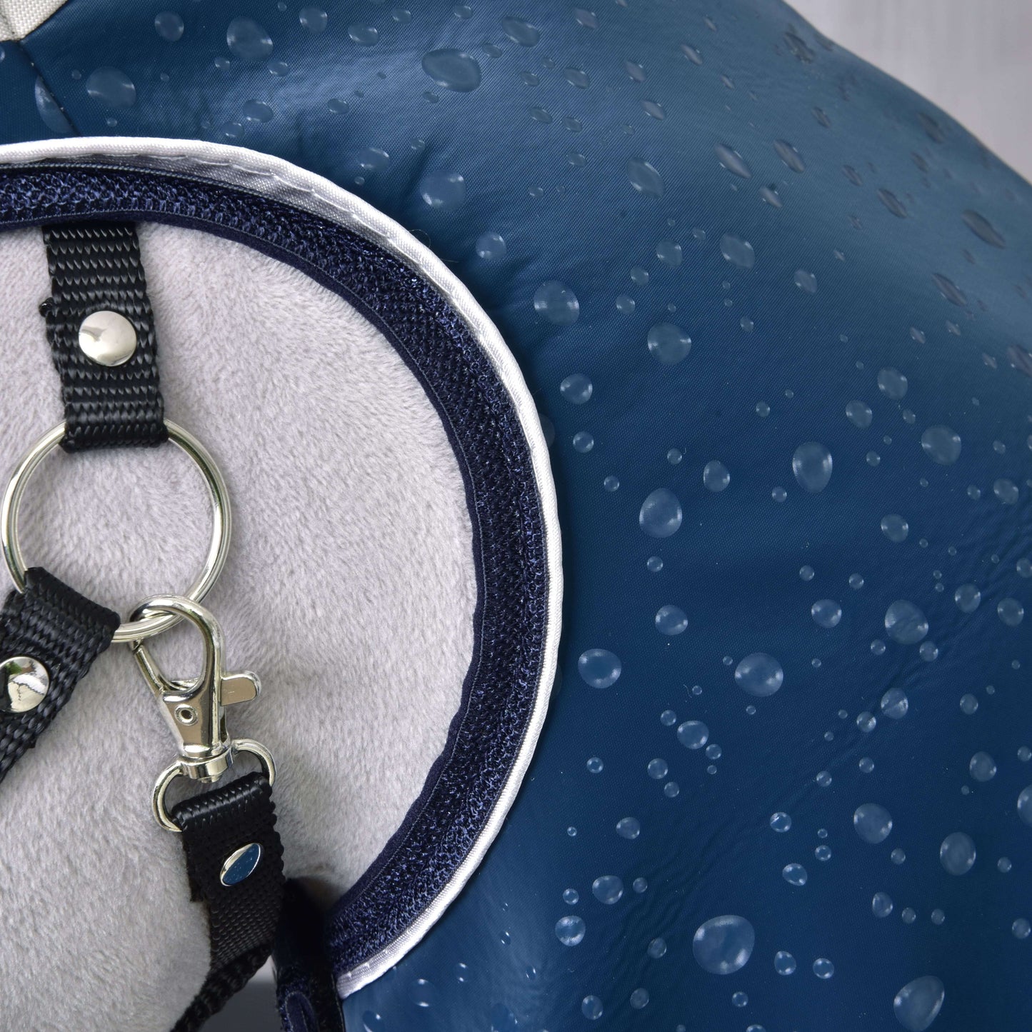 Gros plan sur l’Imperméable Derby de Hobby Horse LarDen, couverture de cheval bleue imperméable pour tous les temps avec gouttes d’eau, doublure gris clair douce et bouclerie métallique sur sangles noires.