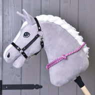 The Hobby Horse LarDen Cordeo pink stripe, featuring a gray plush horse head with a white mane, black bridle, and pink-and-white cordeo on a wooden stick, is ideal for practicing bridleless riding against a gray wooden wall.