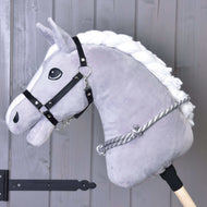 The Hobby Horse LarDen "Cordeo silver stripe" is a plush gray hobby horse with a white mane, black bridle, and handmade gray-and-white cordeo, shown against wood planks with black metal hardware.