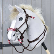 Graues Hobby Horse mit Plüschkopf, weißer Mähne und dunklen Augen trägt das Zaumzeug und Halfter für Hobby Horse Seilset York von Hobby Horse LarDen mit roten und weißen Akzenten, vor grauem Holzhintergrund.