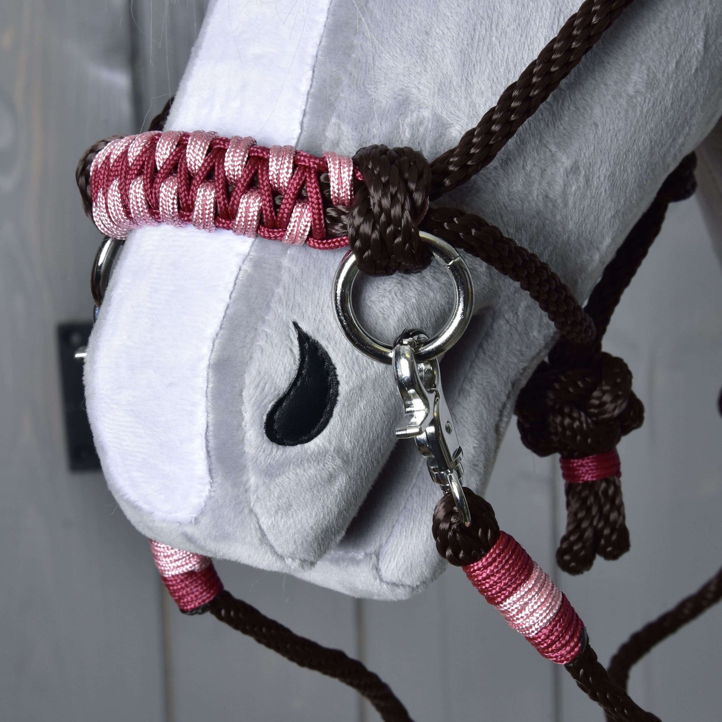 Gros plan sur une tête blanche en peluche Hobby Horse LarDen, avec l’Ensemble de corde York, un licol tressé marron et rose avec anneaux métalliques, et détail de naseau brodé noir.