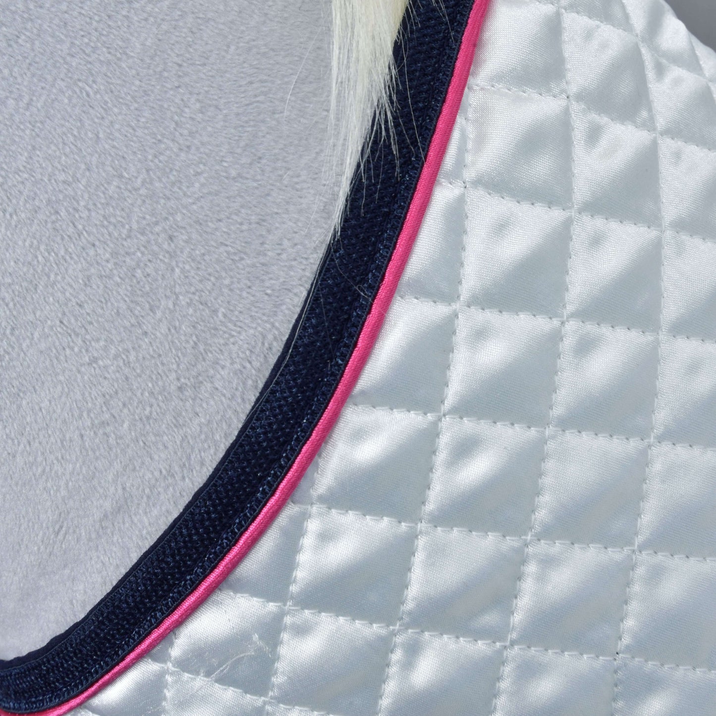 Gros plan sur l'Ensemble Belle Étoile de Hobby Horse LarDen : tissu blanc matelassé avec bordure bleu marine et rose, drapé sur une surface duveteuse gris clair. Une petite section de poils blancs apparaît en haut.