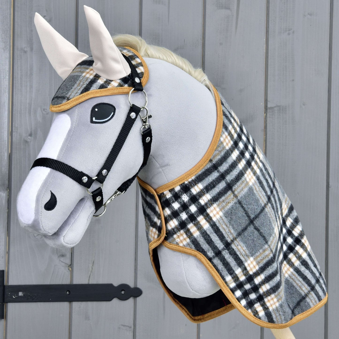 The Hobby Horse LarDen Set England Grey features a gray plush hobby horse with black bridle and reins, plus a plaid blanket and matching ear bonnet, creating a charming decoration against a wooden backdrop.