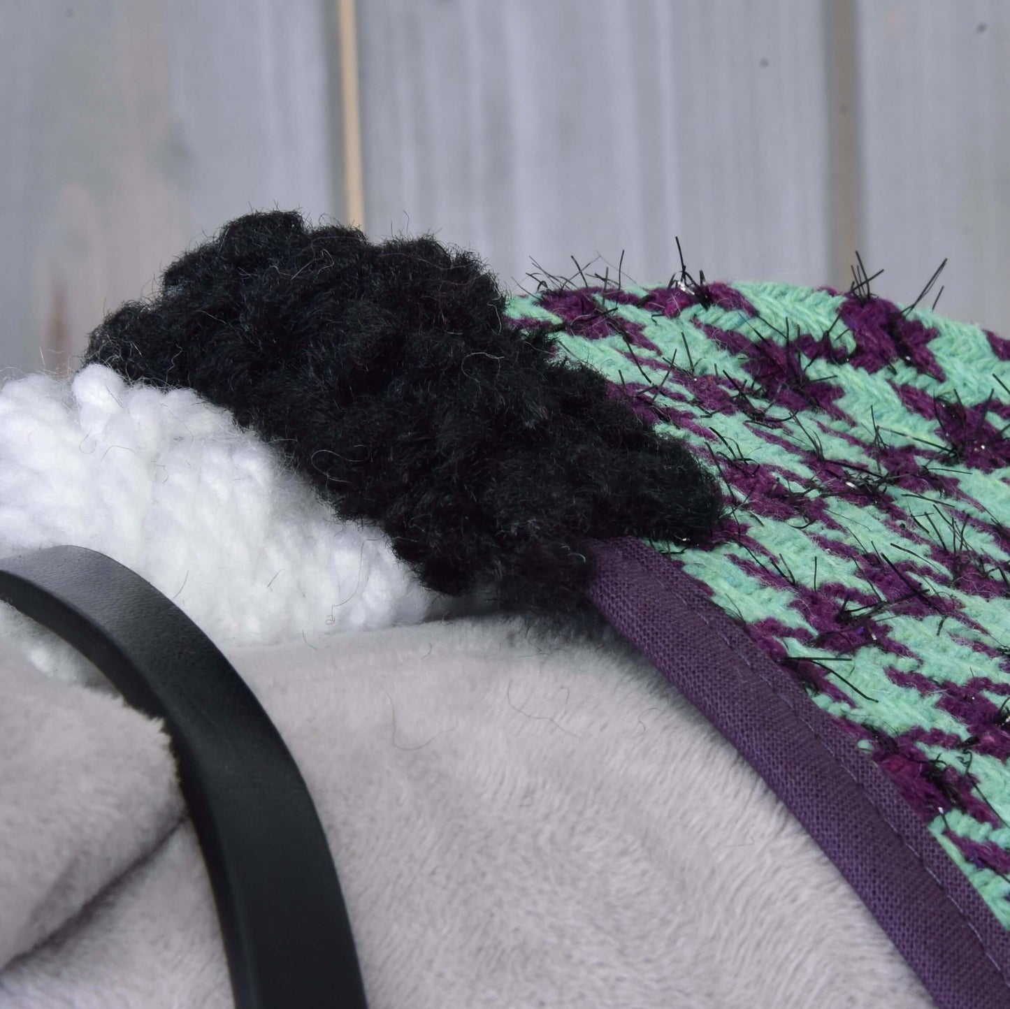 Nahaufnahme des Kopfes von Set Harmony Green von Hobby Horse LarDen mit schwarz-weißer Garnmähne, grün-violettem strukturiertem Stoff, grauer Plüschoberfläche und schwarzem Halfterriemen vor Holzhintergrund.