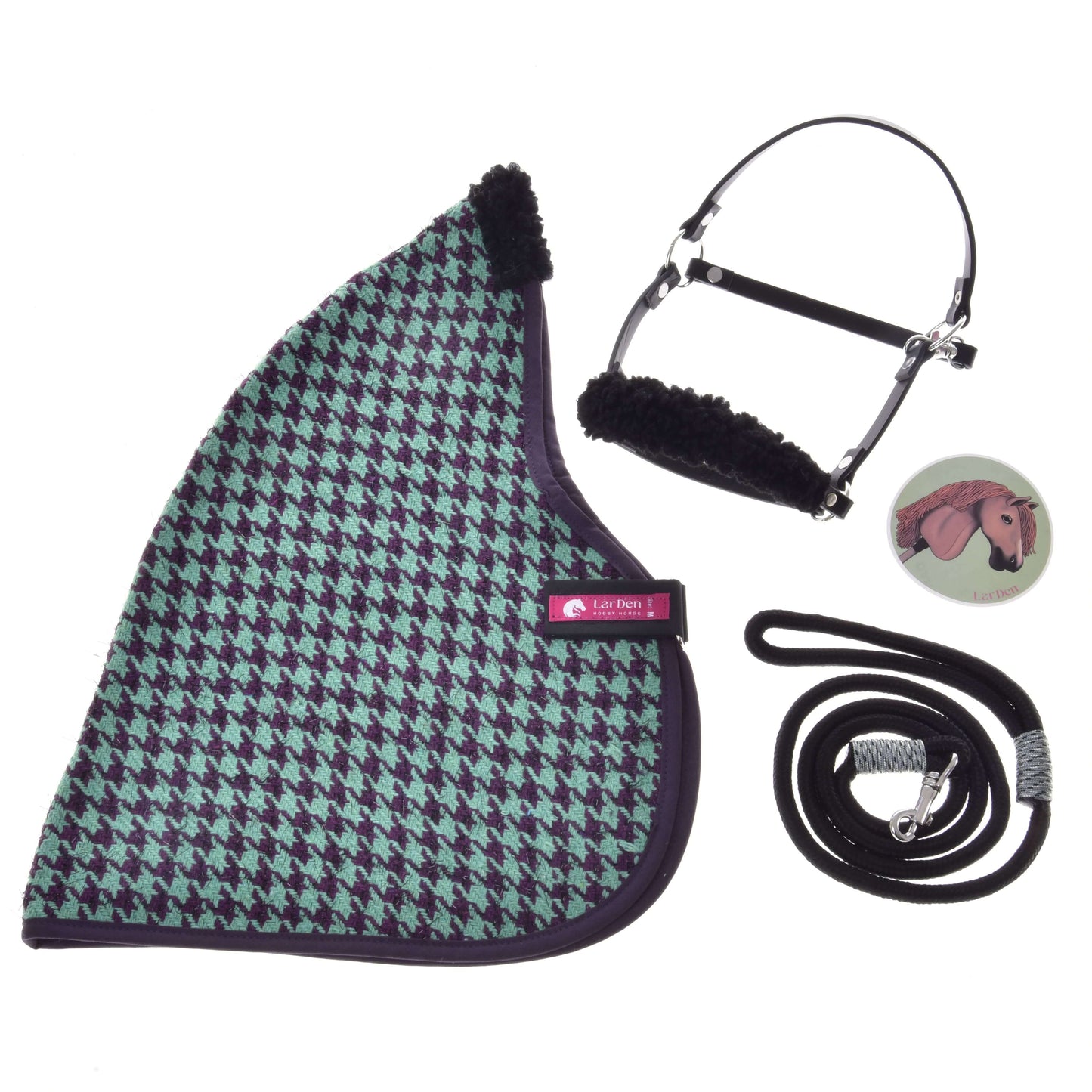 Flatlay des Set Harmony Green von Hobby Horse LarDen: eine grün-schwarze Stalldecke mit Hahnentrittmuster, ein schwarzes Halfter für Hobby Horse mit Fleecepolsterung, ein schwarzer Führstrick mit silbernem Clip und ein runder Pin mit Pferdeillustration.
